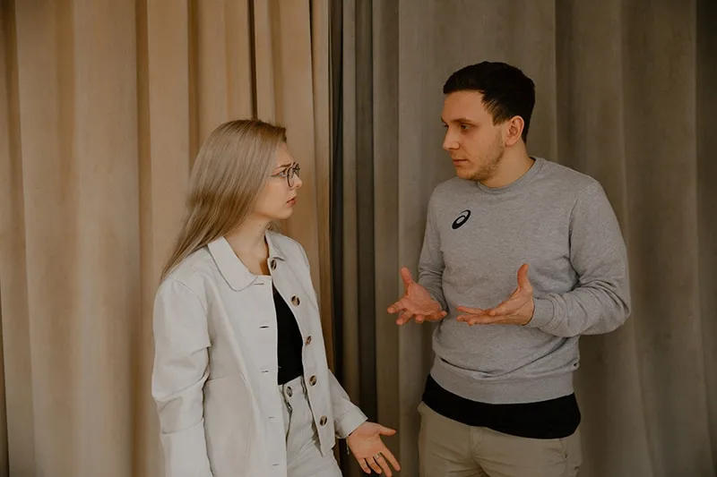 a man arguing with a woman while standing near the curtain together
