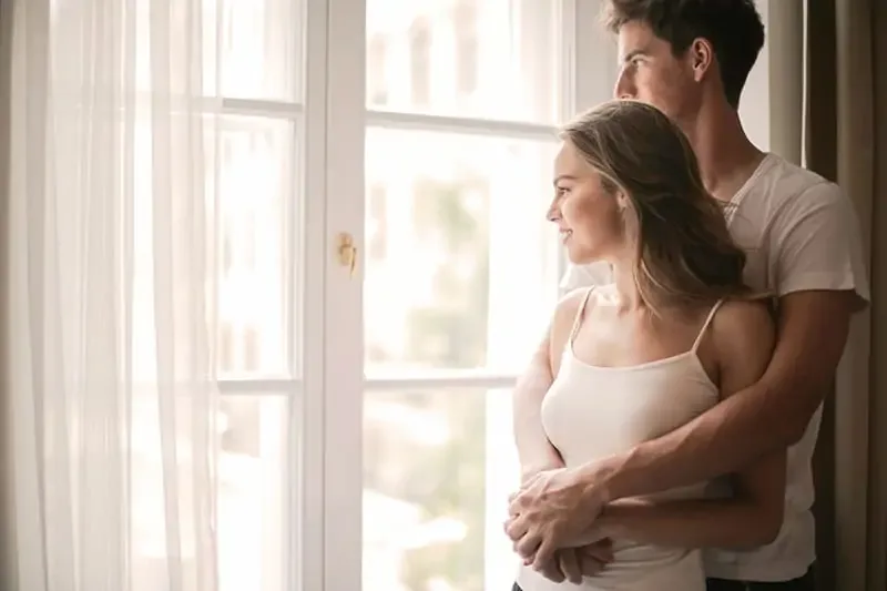a man embracing a woman while standing together near the window