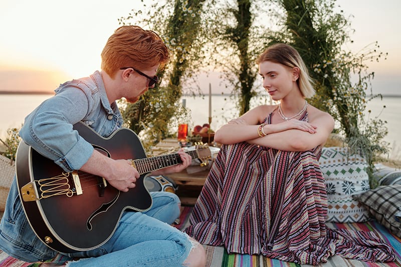 a man playing the guitar for his girlfriend while having a romantic dinner at the beach