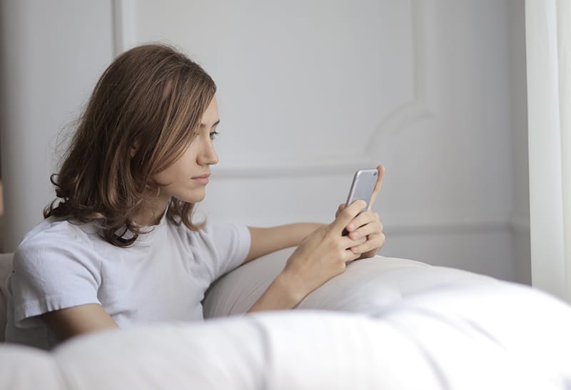 a serious woman texting on her smartphone while sitting on the couch alone