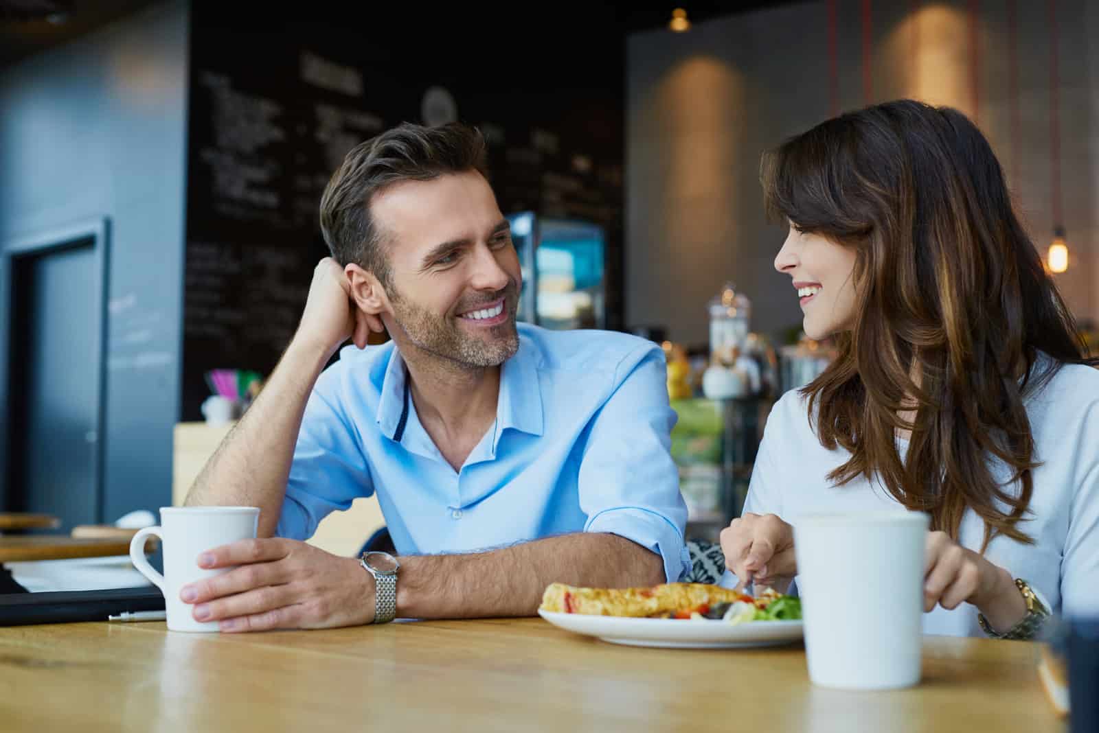 una coppia sorridente seduta a un tavolo che fa colazione parlando