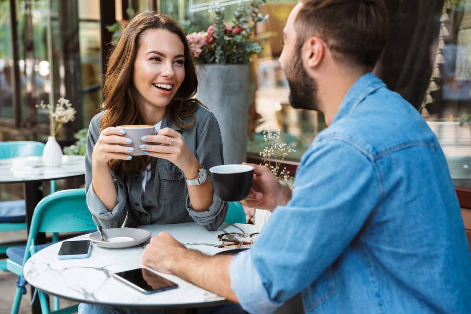 um casal sorridente sentado numa mesa a beber café e a conversar