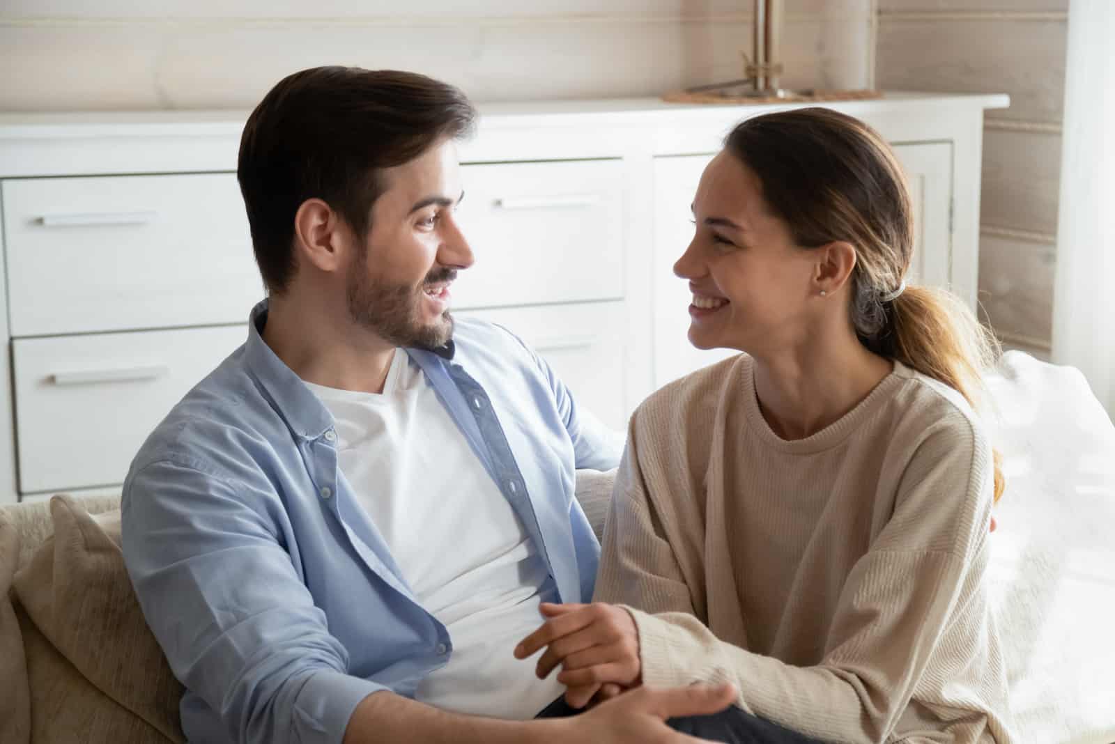 a smiling couple sitting on the couch and talking