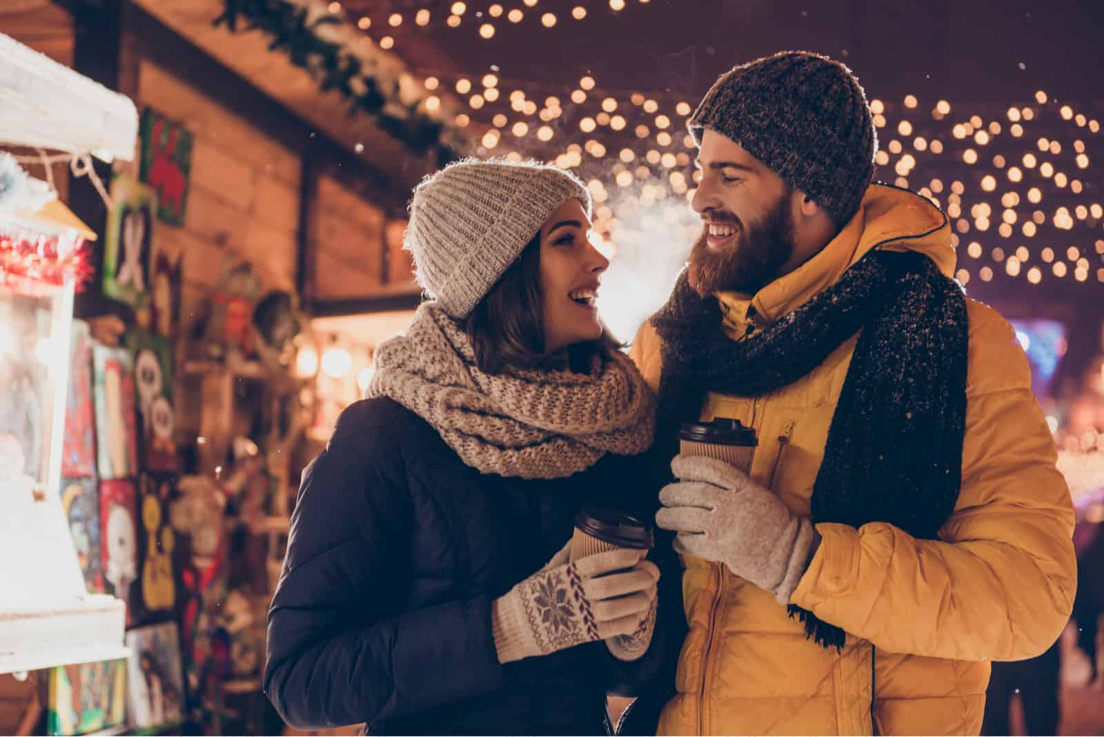 a smiling man and woman holding coffee in their hands and looking at each other