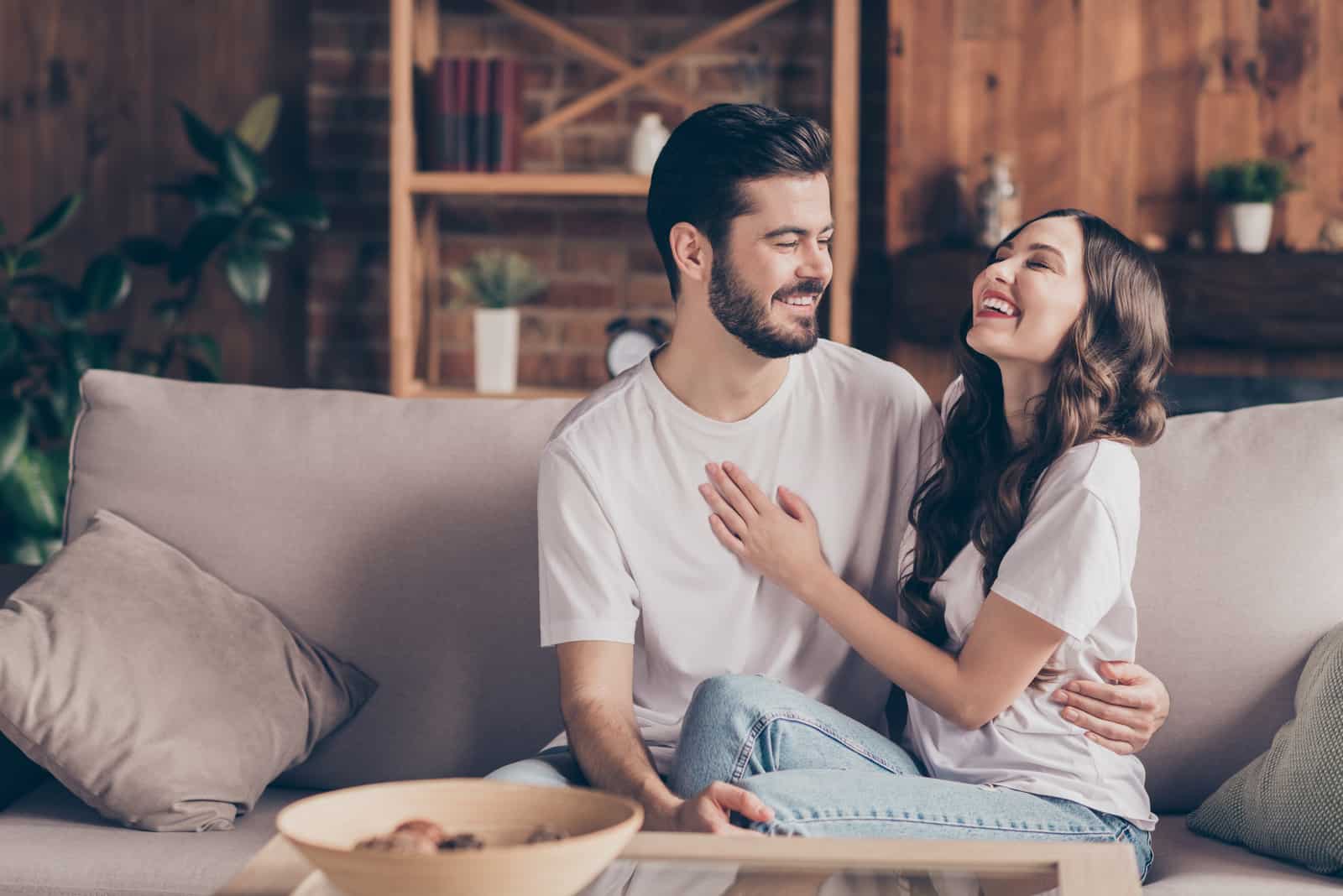 a smiling man and woman sit on the couch and laugh