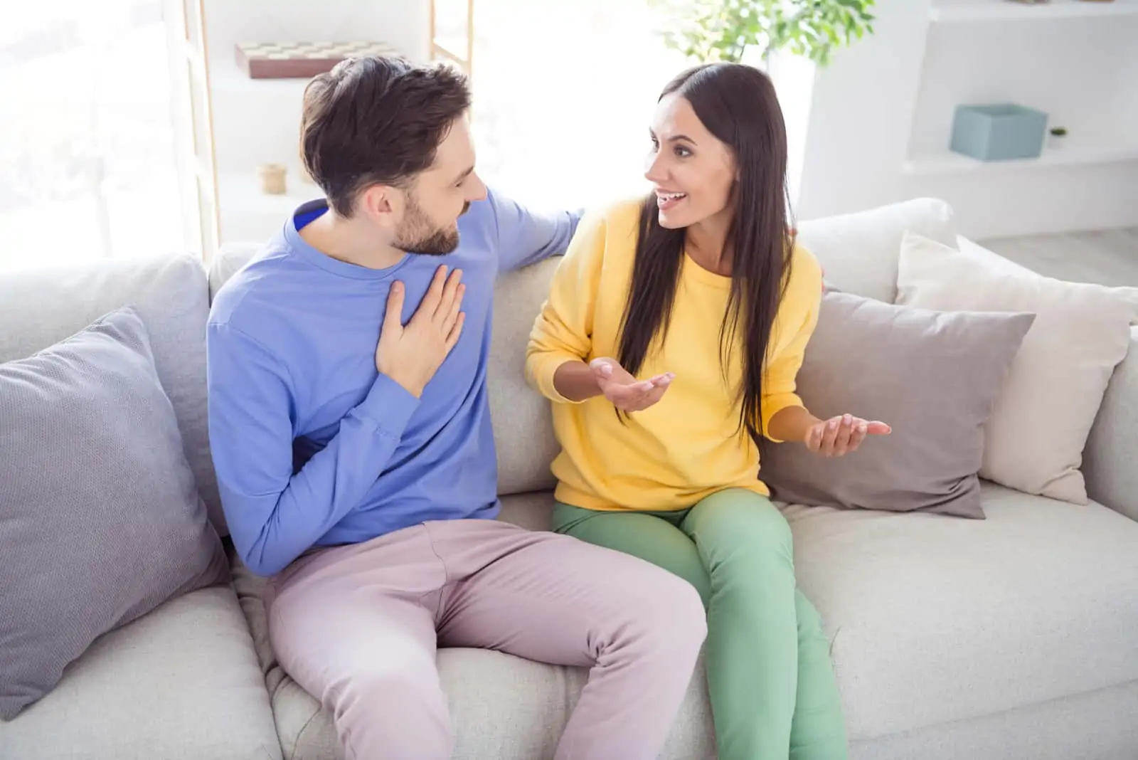 a smiling man and woman sit on the couch and talk