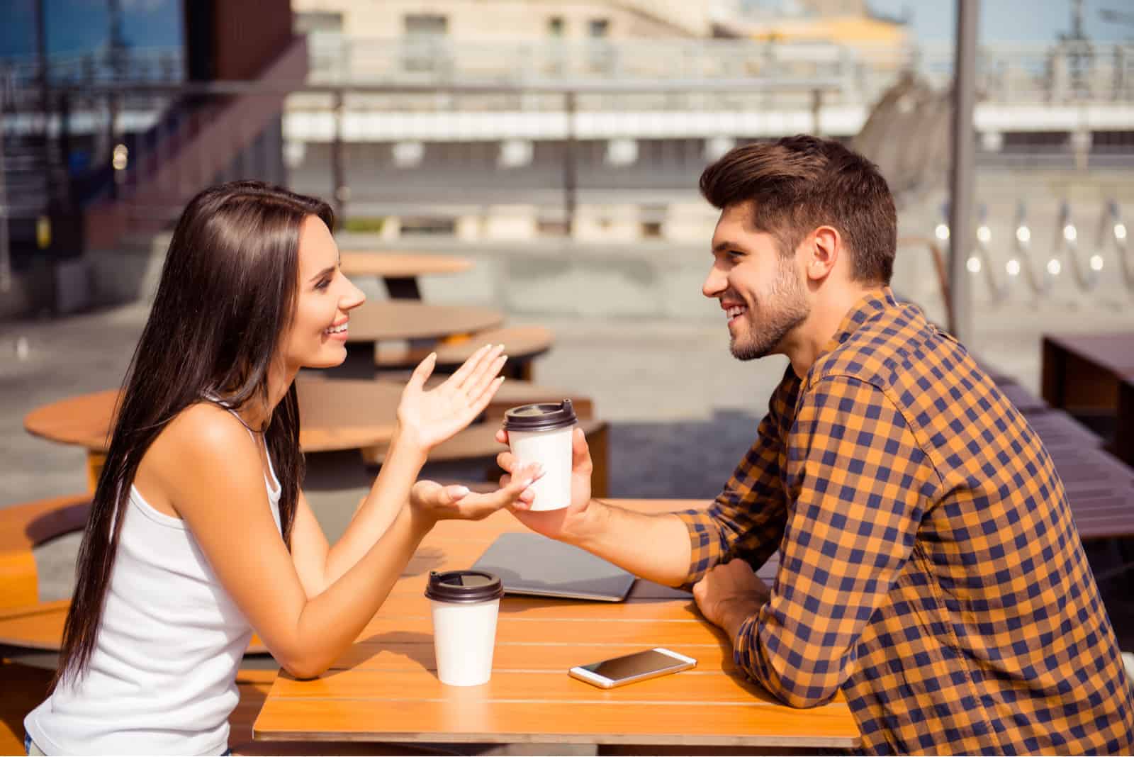 a smiling man and woman sitting outdoors having coffee talking