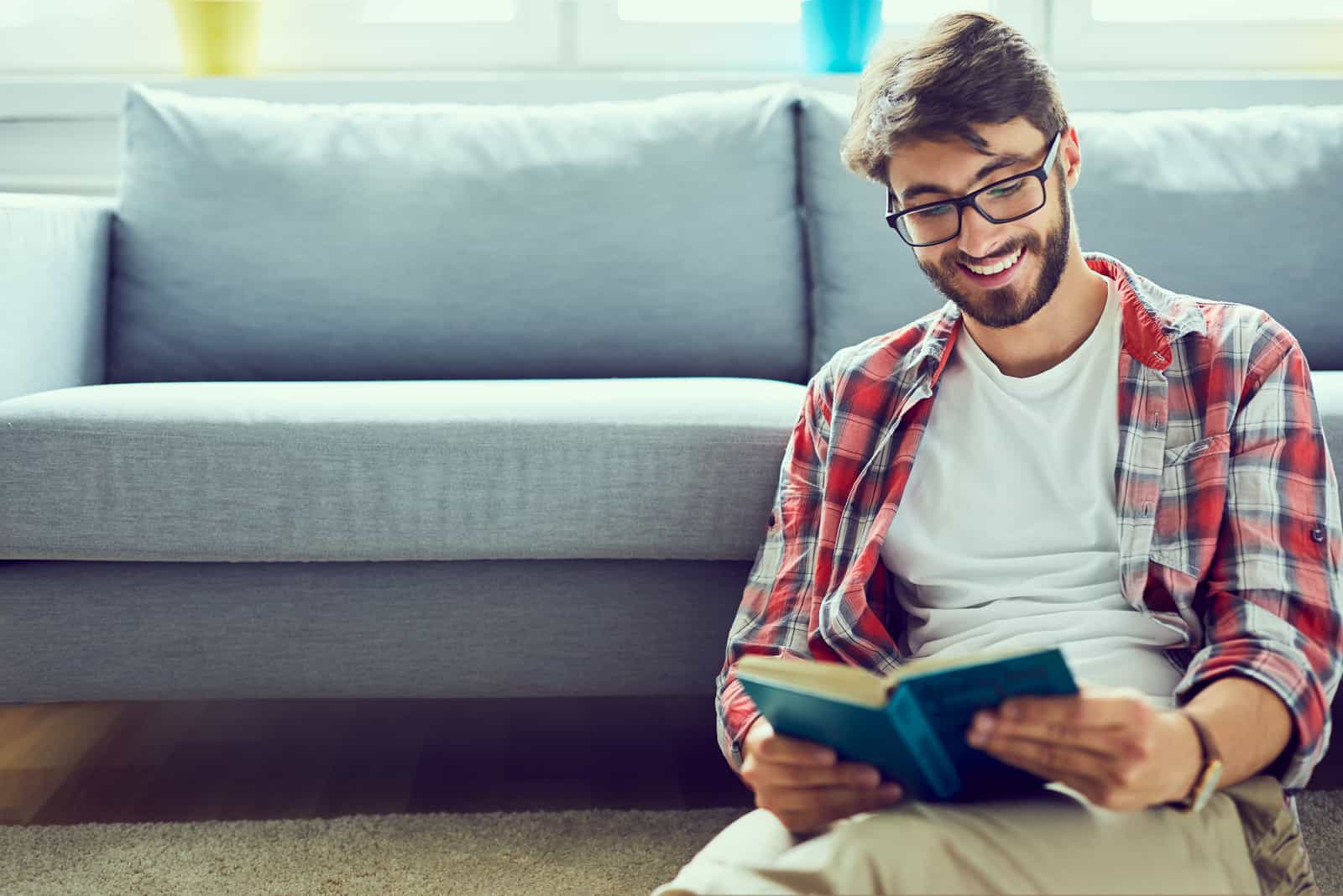 a smiling man sits on the floor and reads a book