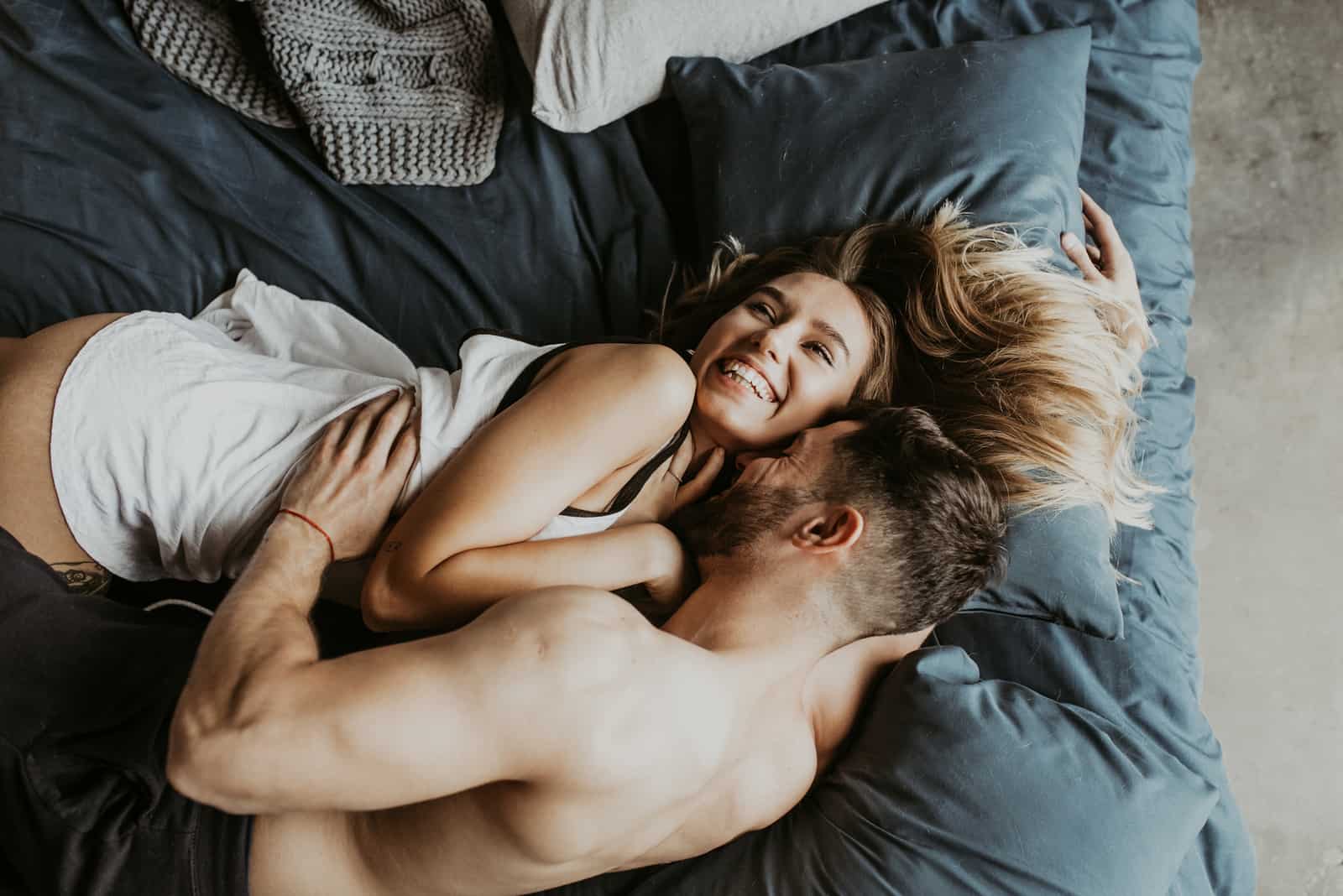 a smiling woman lies in bed with a man