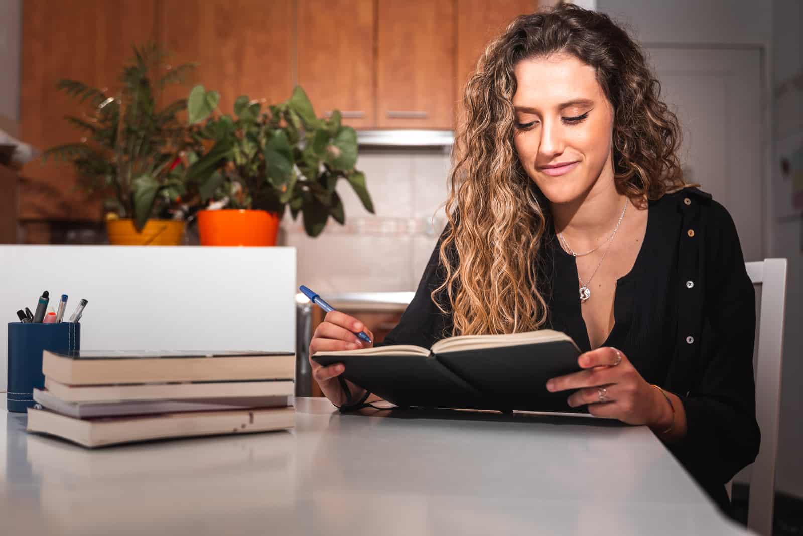 a smiling woman sits at a table and writes