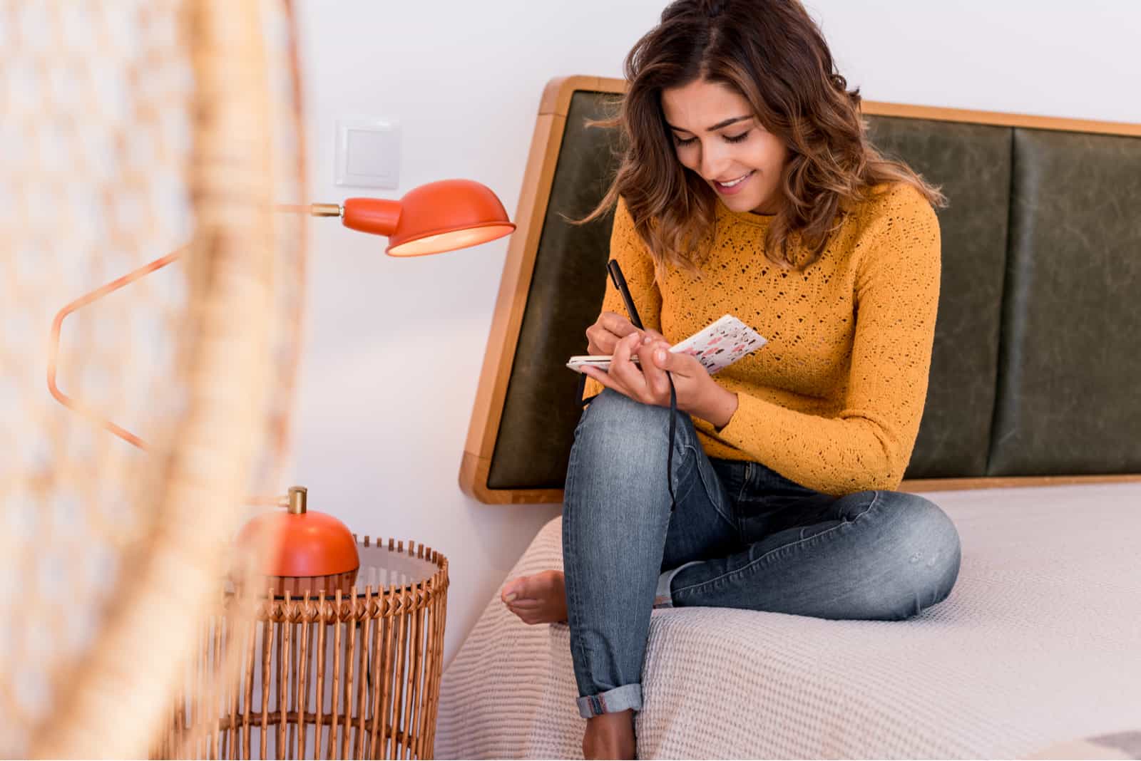 a smiling woman sits on the bed and writes a diary