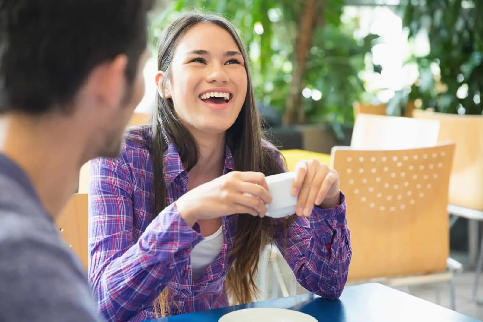 a smiling woman talking to a man while drinking coffee