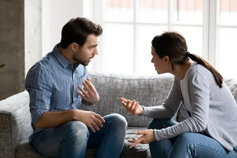 a stressed man arguing with his wife sitting together on the couch at home