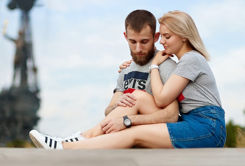 una donna che abbraccia il suo ragazzo mentre sono seduti insieme sulla strada
