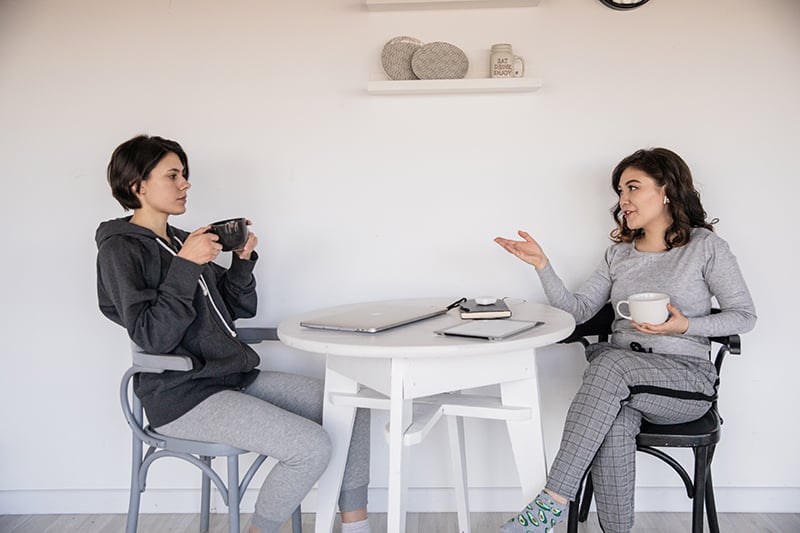 a woman gesticulating with hand and advising her friend while having coffee together