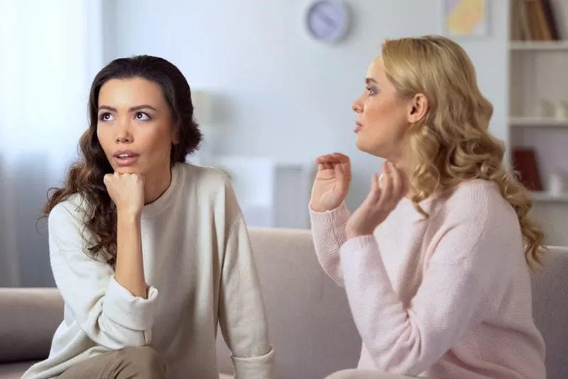a woman ignoring her female friend talking to her while sitting on the couch together