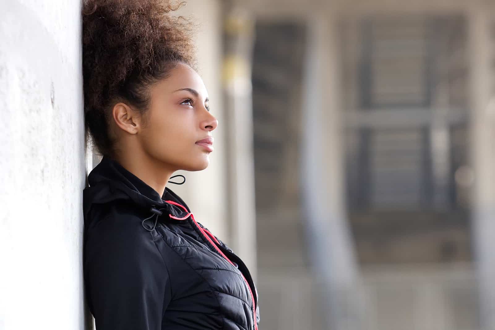 a woman with frizzy hair stands leaning against the wall