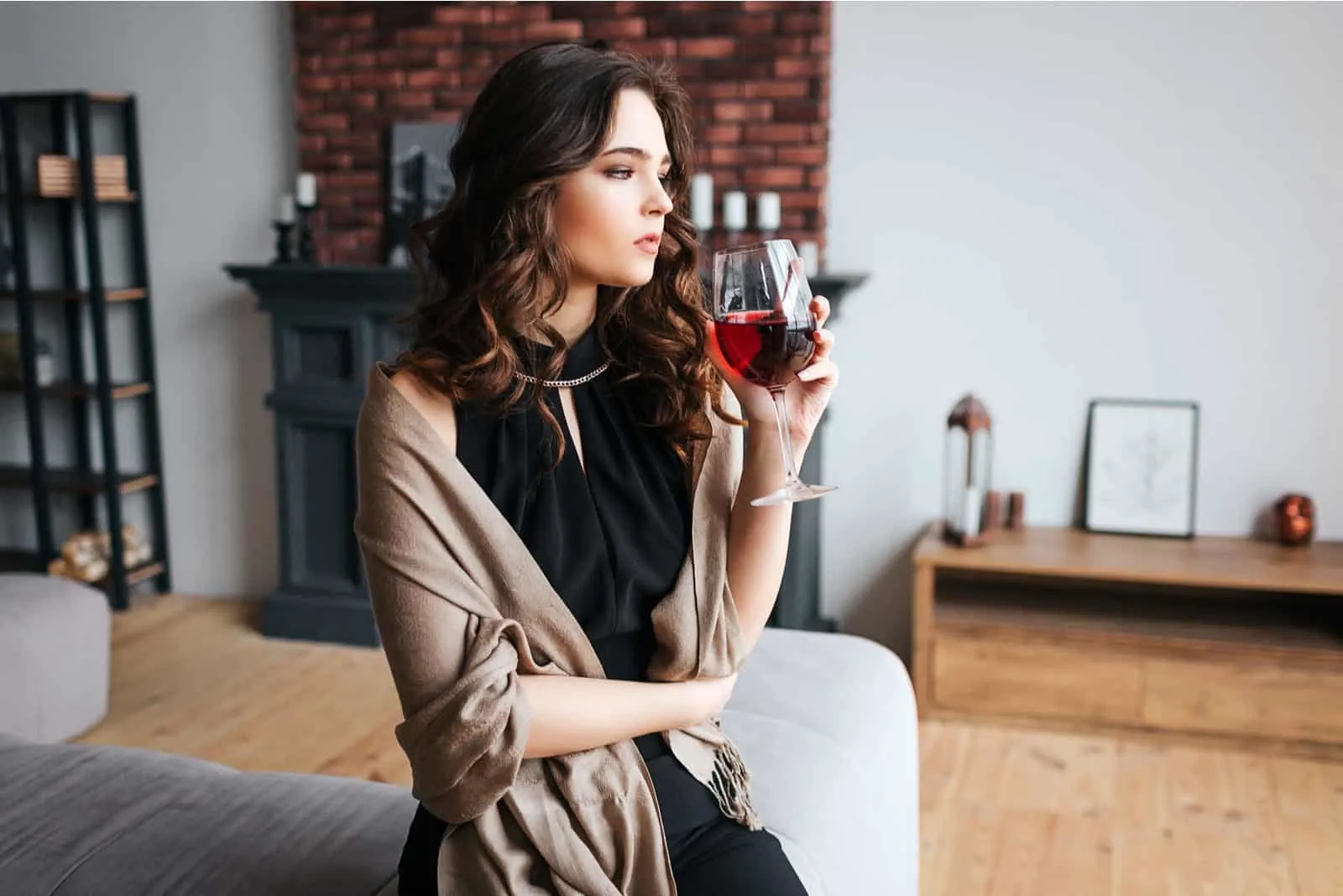a woman with long black hair leaning against the couch drinks wine