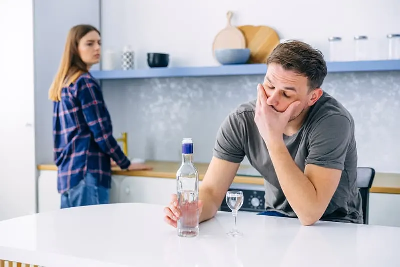 alcoholic sitting with a bottle of vodka while wife looking at him