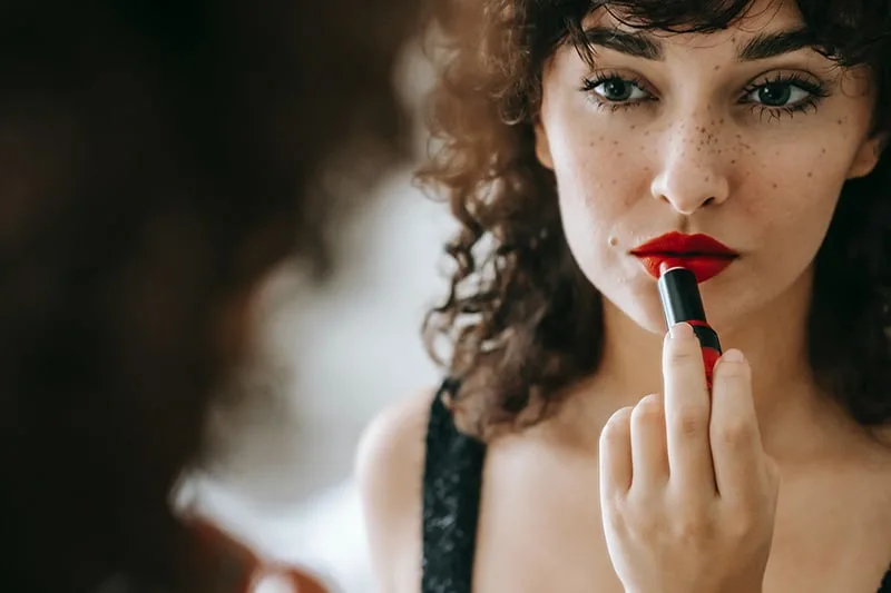 confident woman applying lipstick in front of the mirror