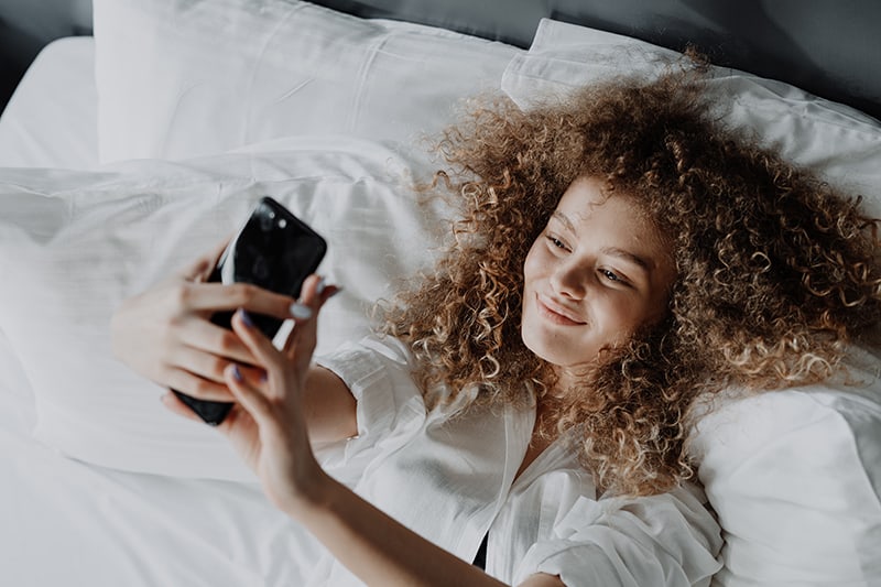 confident woman lying in the bed and taking selfie with phone