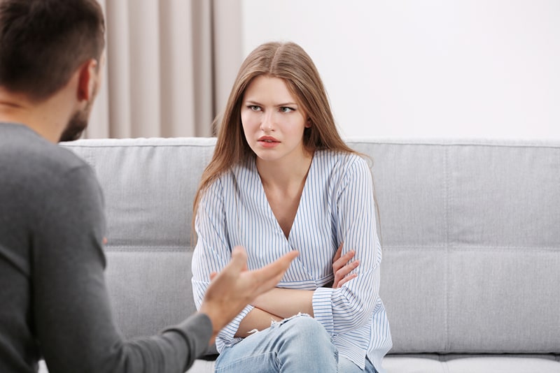 confused woman listening a man arguing with her while sitting on the couch