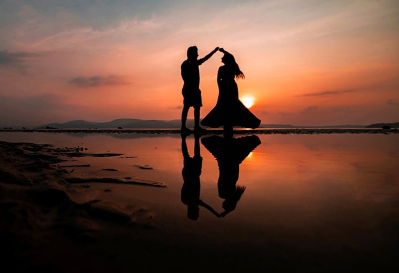 casal a dançar na praia durante o pôr do sol