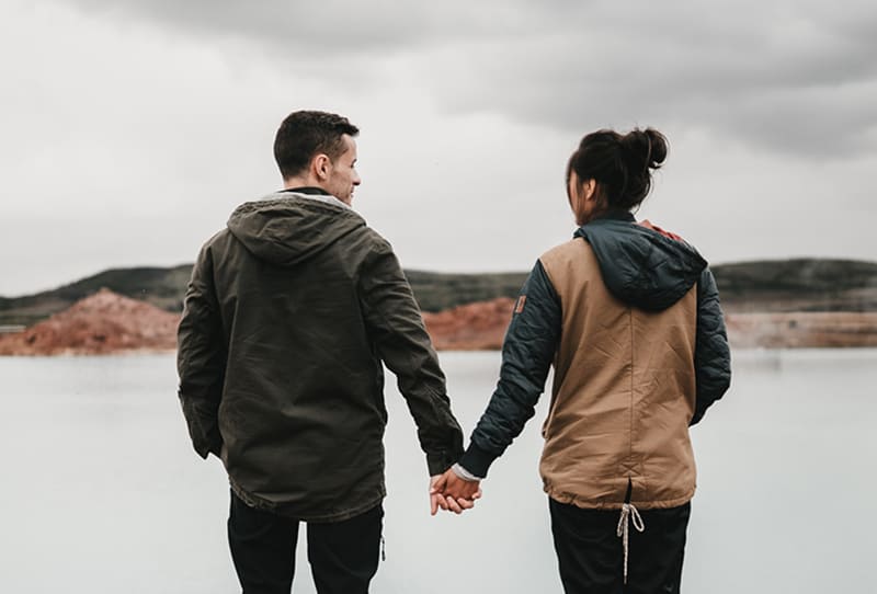 couple holding hands standing near the body of water 