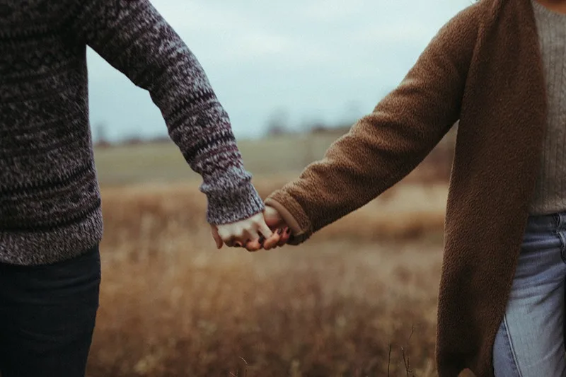 couple holding hands walking in the field