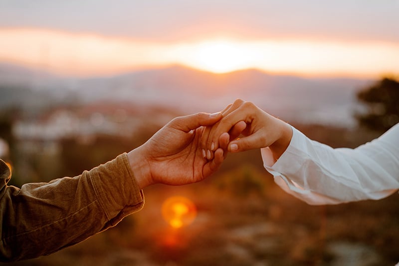 casal de mãos dadas no campo ao pôr do sol