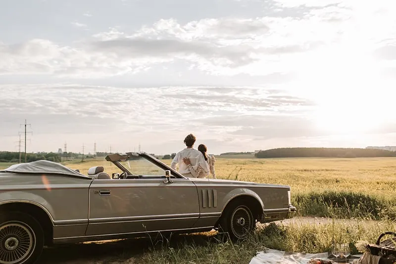 couple leaning on the car observing sunset in the field
