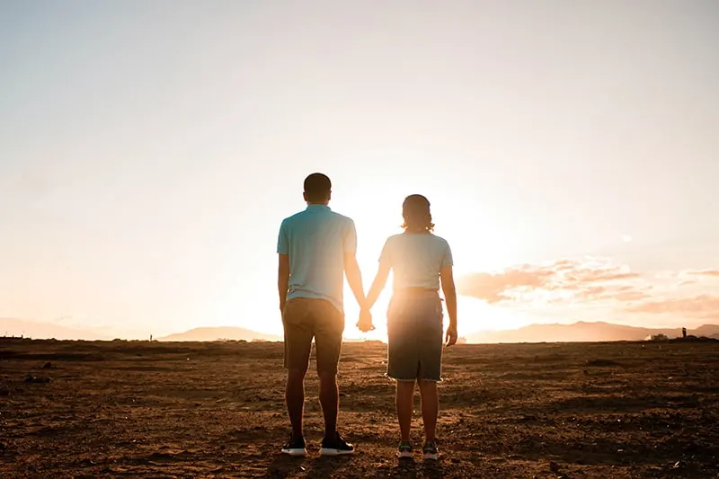 couple standing in the field and holding hands observing sunset