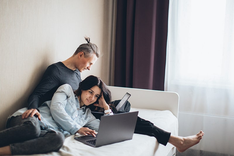 coppia che lavora insieme al proprio laptop seduta sul letto