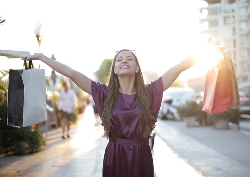 mulher feliz levantou as mãos enquanto segurava sacos de compras