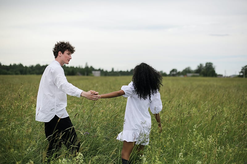 loving couple holding hands while walking in grass field