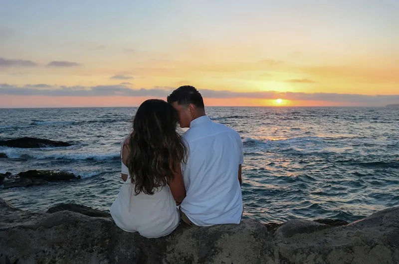 loving couple sitting on the rock near the sea during sunset