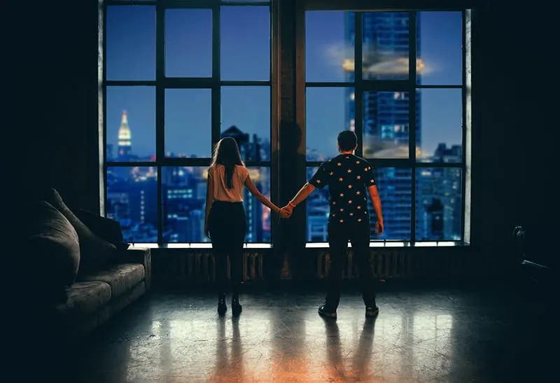 man and a woman holding hands standing in front of the window in apartment