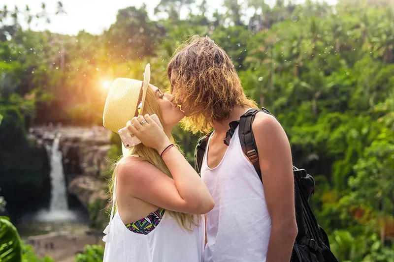 man and woman kissing near the waterfall