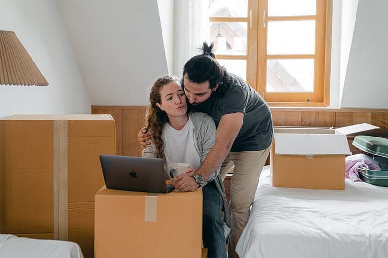 hombre abrazando a su novia por la espalda mientras ella se sienta delante del portátil