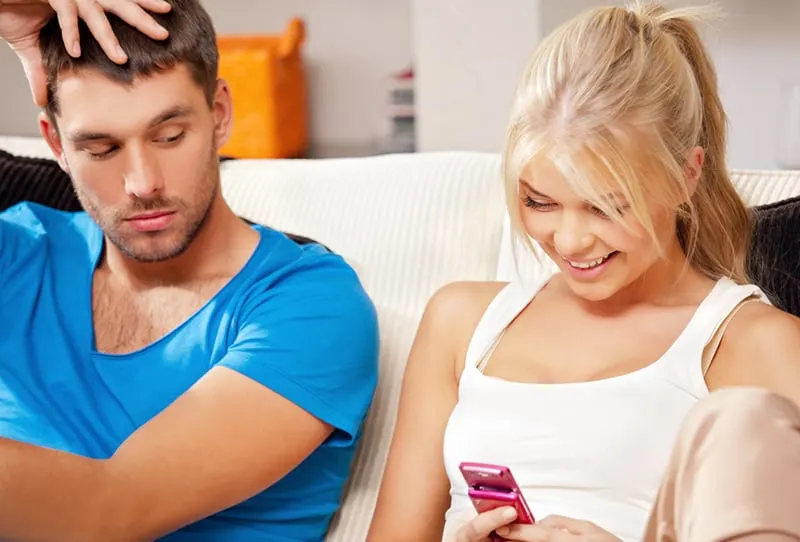 man looking at the phone of smiling girlfriend while she using it
