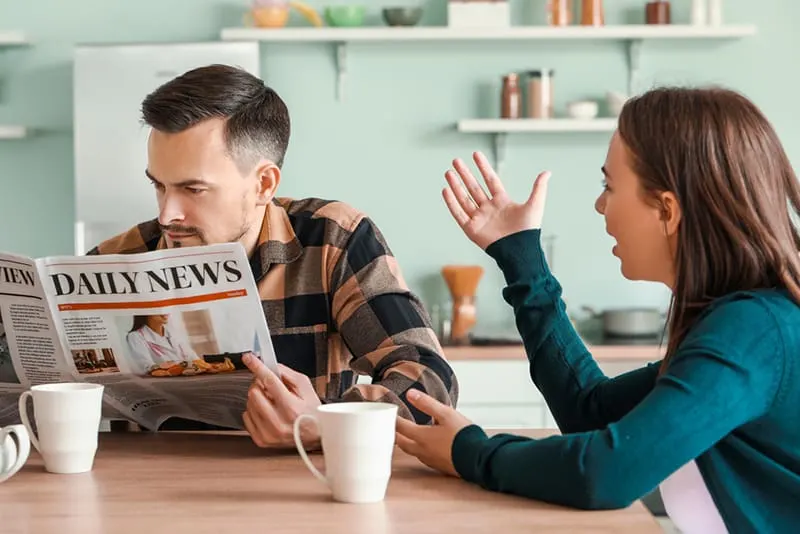 man reading newspaper ignoring his wife talking to him