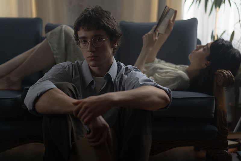 man sitting on the floor and listening to his girlfriend reading a book lying on the couch
