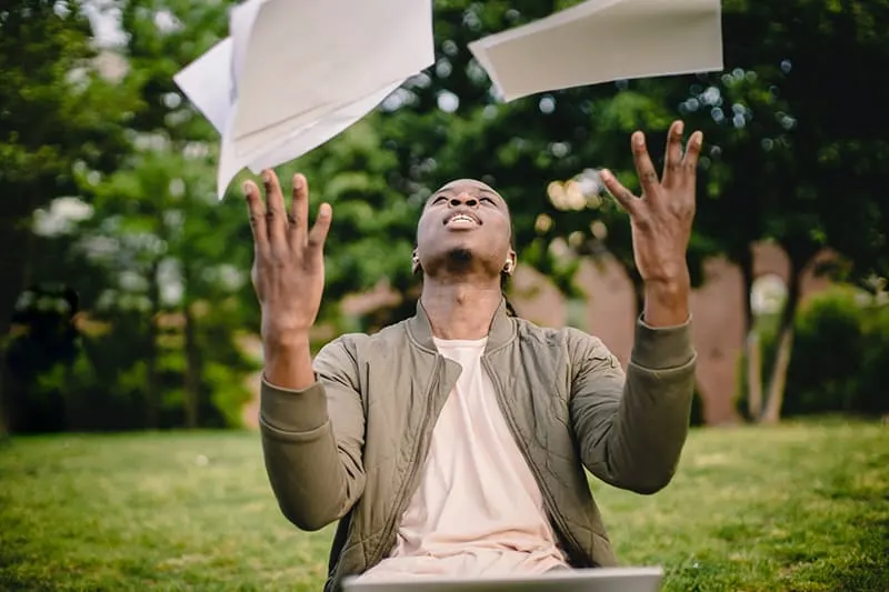 man tossing papers in the air sitting on the grass