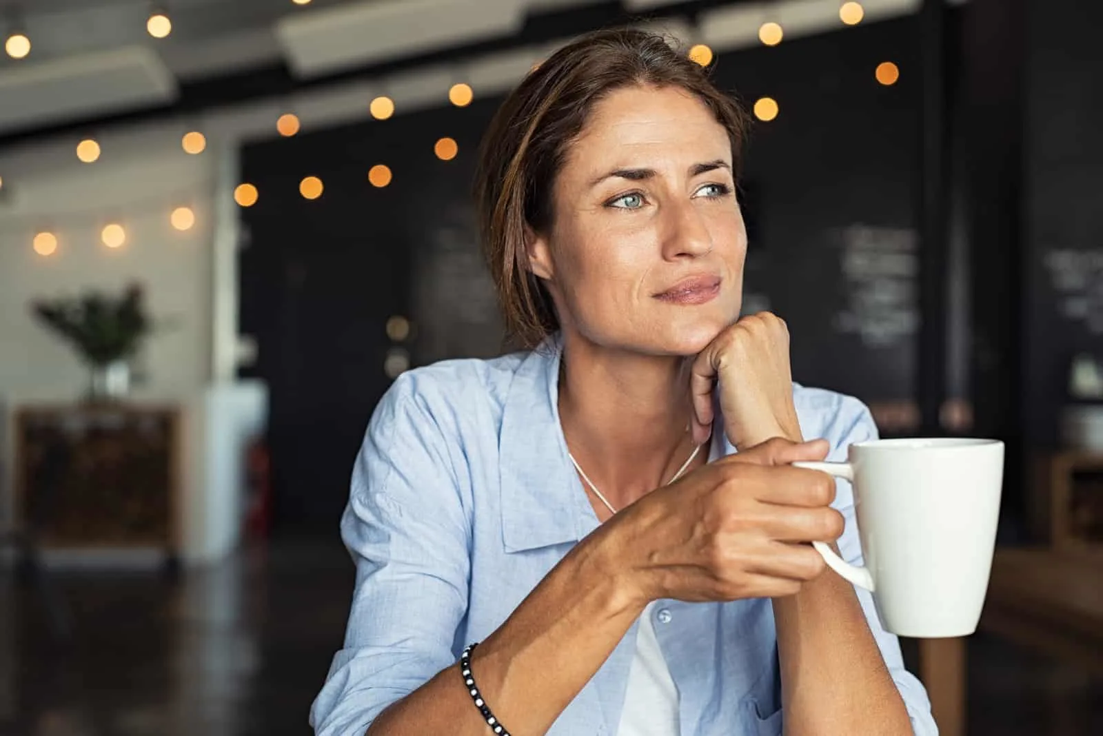 mature woman sitting in cafeteria holding coffee mug