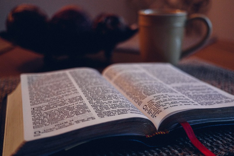 opened bible on black mat beside gray mug