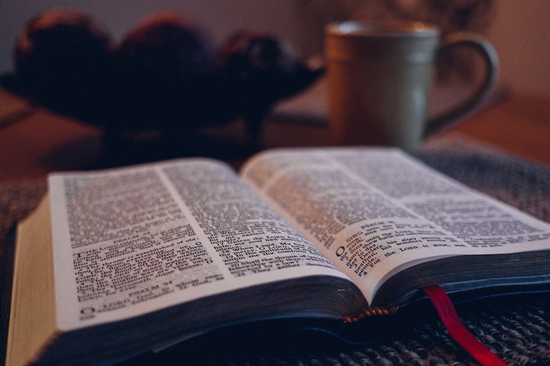 biblia abierta sobre alfombra negra junto a taza gris