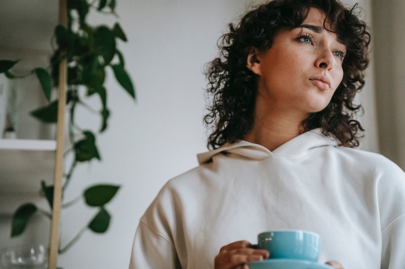 mujer pensativa con una taza de té en la mano mirando a un lado