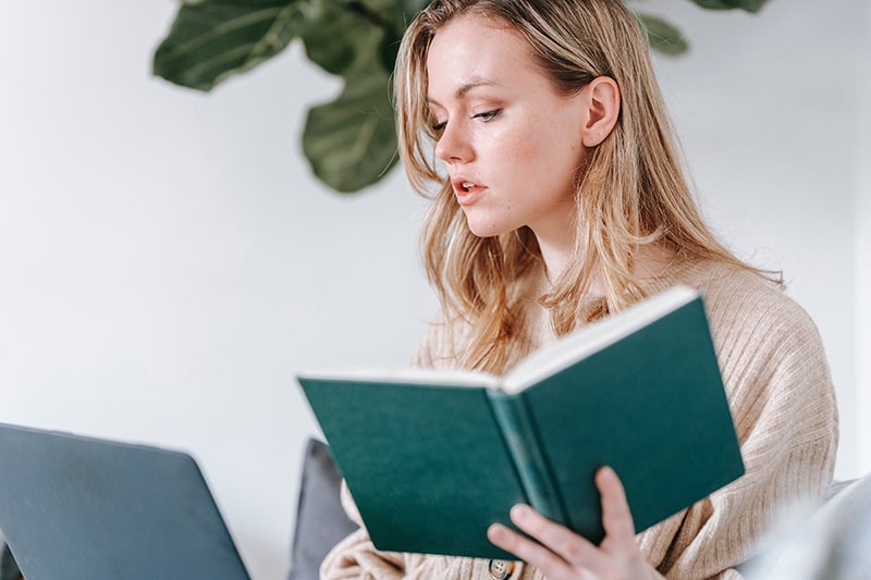 pensive woman holding book and looking at laptop
