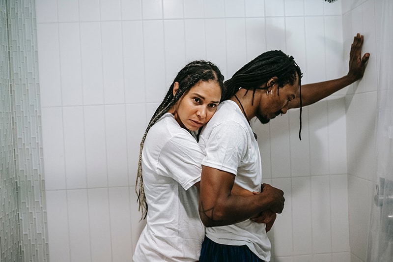 pensive woman hugging his husband from the back standing together in the bathroom