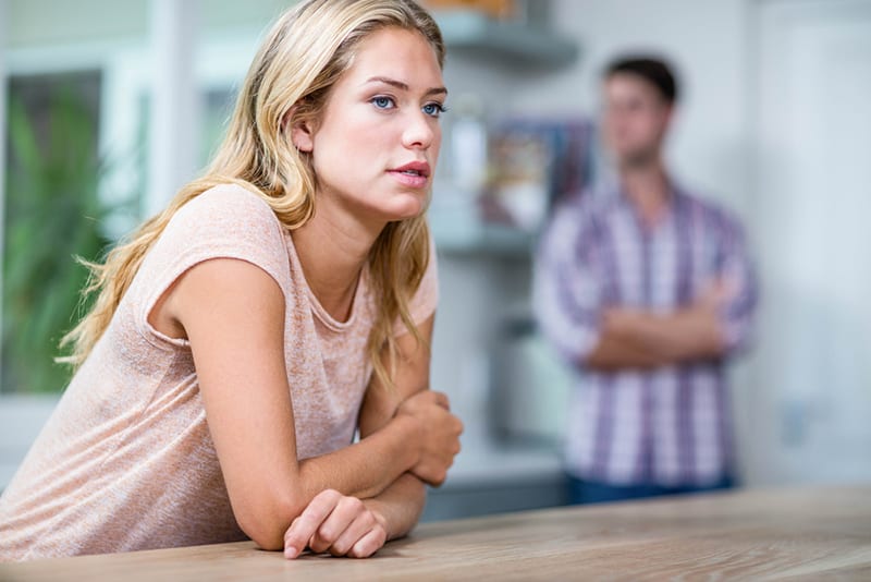pensive woman questioning herself in front of her husband standing in the kitchen